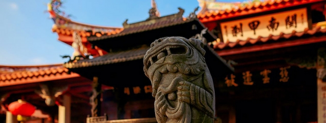 A statue representing a Japanse deity is at the center, a temple is in the background