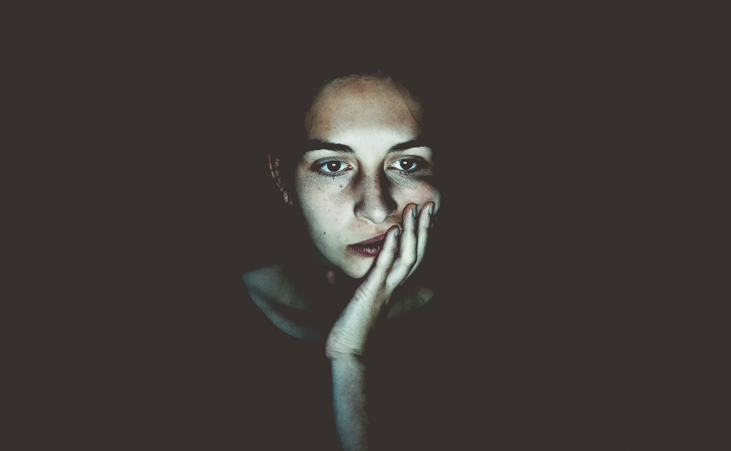 A woman looking bored over a dark background holds her head in her hand